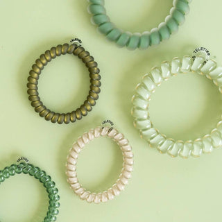 TELETIES spiral coil hair ties in assorted nature-inspired matte and glossy finishes on green background