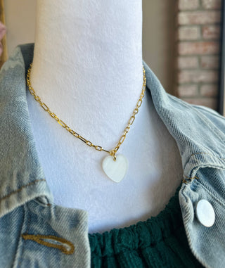 Mother of pearl heart pendant on gold chain necklace displayed on mannequin wearing denim jacket.