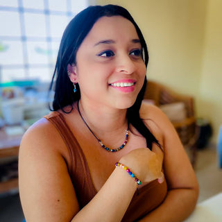 Woman wearing the Alegria Accessories Mountain Breeze Bracelet with matching colorful beaded necklace, smiling indoors.