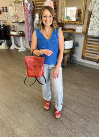 Woman wearing light grey cropped straight jeans with blue knit top in boutique setting