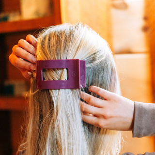 Hands clipping a large rectangular hair clip into long blonde hair from behind.