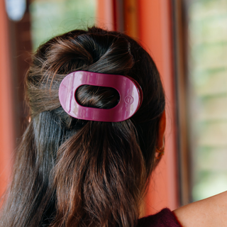 Woman wearing a flat round hair clip securing a half-up hairstyle, back view.