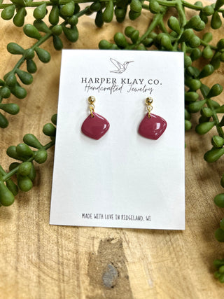 Harper Klay Co handcrafted mulberry-colored clay earrings with gold studs displayed on branded card with green plants.