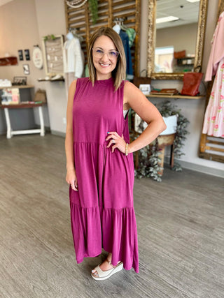 Woman modeling a sleeveless tiered maxi dress in a boutique setting with natural lighting.