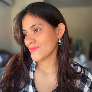 Woman wearing Alegria Accessories Mum Earrings, gold flower-shaped drop earrings with pearl center.