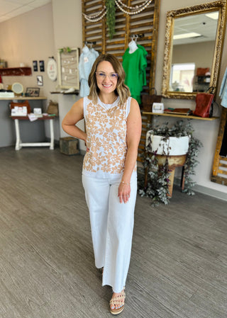 Woman wearing floral patterned sleeveless tank top with white pants in boutique setting