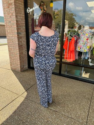 Woman wearing navy patterned jumpsuit with ruffled sleeves standing outside boutique storefront