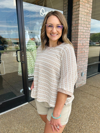 Woman wearing a loose, open-knit striped top with short sleeves, styled casually outdoors.