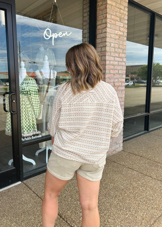 Woman wearing a textured knit top with shorts, shown from behind outside a boutique storefront.