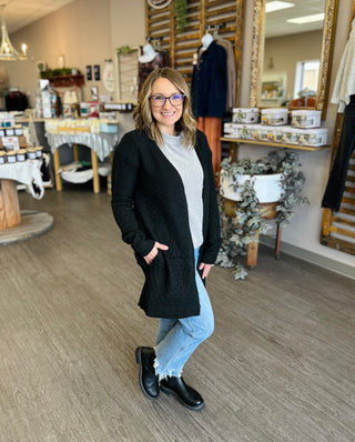 Woman wearing black knit cardigan with pockets in boutique store setting