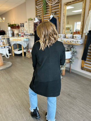 Woman wearing dark knit cardigan from behind in salon, showing relaxed fit and styling details.