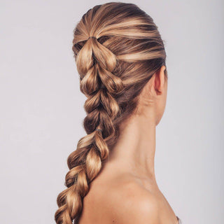Woman with long blonde highlighted hair styled in an intricate braided ponytail using elastic hair ties.