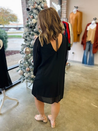 Woman wearing black dress with open back detail standing in boutique store