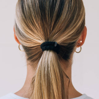 Woman wearing sleek low ponytail secured with black TELETIES nylon hair tie, showing smooth gathered hair.