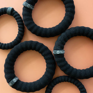Black nylon hair ties with TELETIES branding arranged on peach background