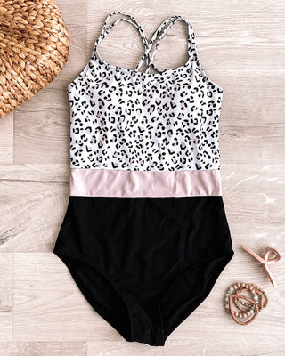 One-piece swimsuit with leopard print top, pink stripe, and black bottom on wooden surface with accessories.