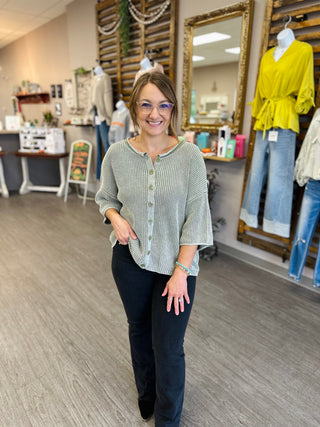 Woman smiling in a ribbed button-front sweater top with three-quarter sleeves, styled with dark jeans.