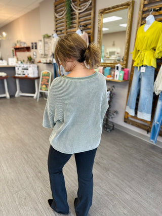 Woman modeling Blu Pepper Olive Charm Sweater Top from behind in boutique setting.