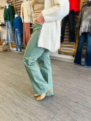 Person wearing olive green wide-leg jeans with frayed hem and white sweater in clothing store