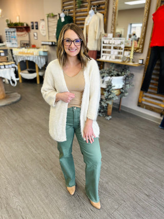 Woman wearing olive green flared jeans with cream cardigan in clothing boutique store setting
