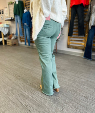 Person wearing olive green flared jeans with frayed hem and cream sweater in clothing store