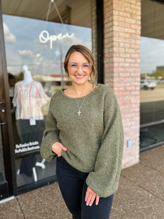 Woman wearing a cozy oversized fuzzy knit sweater with balloon sleeves outside a boutique.