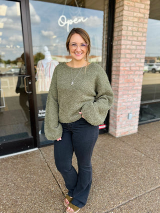 Woman smiling outside boutique wearing a cozy fuzzy knit pullover sweater with dark jeans.