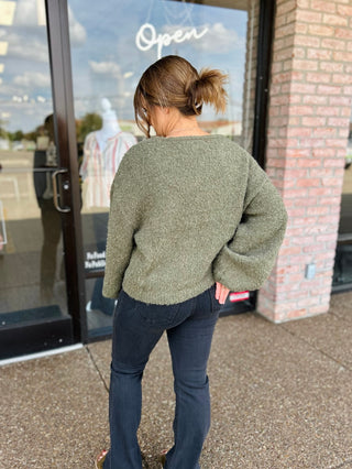 Woman wearing a fuzzy knit sweater with dark flare jeans, back view, outdoors.