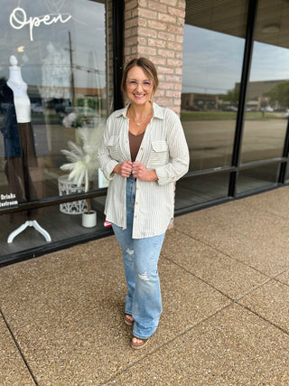 Woman wearing a striped button-down shirt jacket over a tank top with distressed jeans.