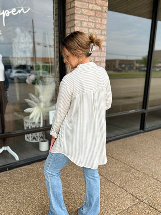 Woman wearing a striped oversized button-down shirt with flare jeans outside a boutique.