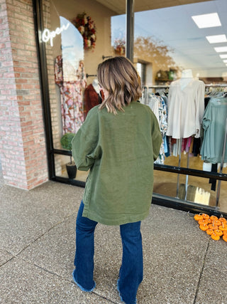 Woman wearing oversized olive green jacket with blue jeans standing outside boutique storefront