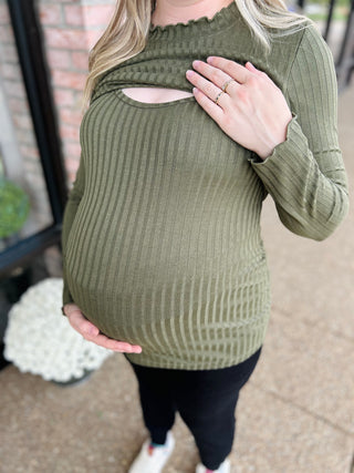 Pregnant woman wearing olive green ribbed knit maternity top with nursing access opening, hands on belly.