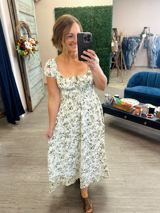 Woman wearing a floral midi dress with puff sleeves, square neckline, and brown sandals.