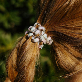 TELETIES hair tie with translucent beaded design holding blonde hair in ponytail against green background.