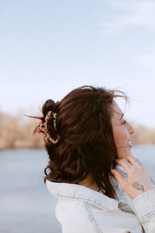 Woman wearing a large tortoiseshell hair clip in wavy brown hair, shown from behind outdoors.