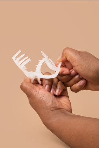 Hands holding a white claw-style hair clip against a peach background