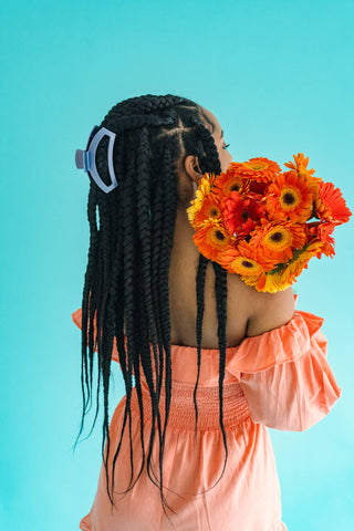 Woman with braided hair wearing TELETIES hair clip while holding orange flowers against turquoise background