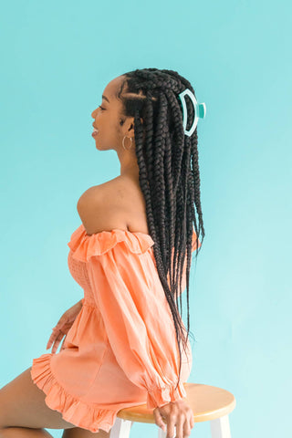 Woman wearing turquoise hair clip with long braids and coral off-shoulder dress against blue background