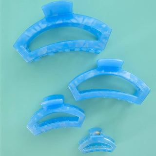 Four blue curved hair clips arranged in descending size order on a mint green background.