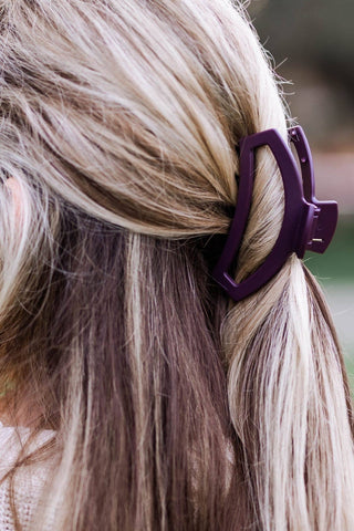 Woman's blonde hair styled in half-up ponytail secured with purple heart-shaped open hair clip.