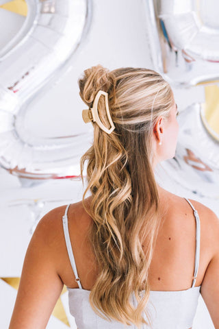 Woman wearing blonde wavy hair in half-up style with champagne-colored open hair clip accessory.