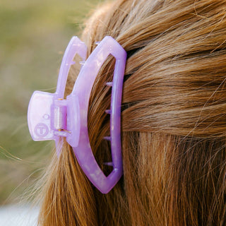 Purple open hair clip holding brown hair in a ponytail, showing the clip's curved design and grip mechanism.