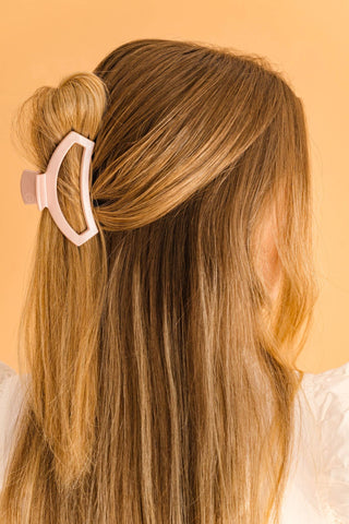 Woman wearing pearly pink open hair clip in blonde hair against orange background