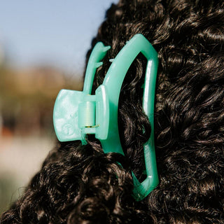 TELETIES open hair clip securing curly dark hair in an outdoor setting