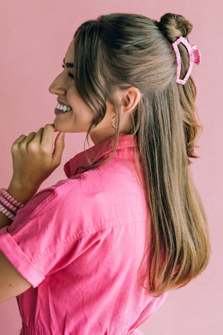 Woman wearing pink hair clip with ribbons in blonde hair against pink background