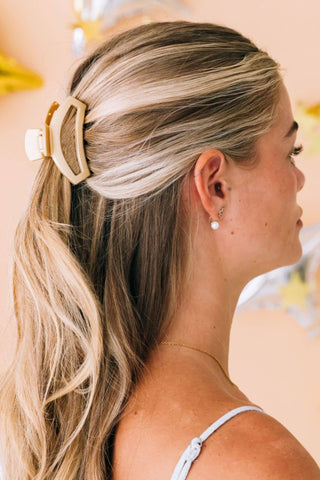 Woman wearing blonde hair in half-up style secured with champagne-colored open hair clip and pearl earrings.