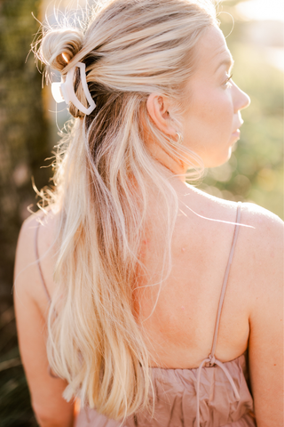 Woman with blonde hair wearing a white hair clip in a half-up hairstyle outdoors.