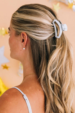 Woman wearing white open hair clip in blonde highlighted hair styled in half-up ponytail