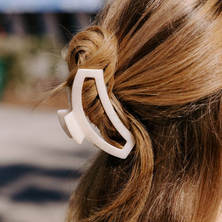 Woman wearing a white open hair clip holding blonde hair in a ponytail