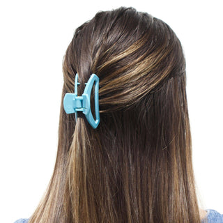 Woman wearing a blue open hair clip holding back brown highlighted hair against white background.